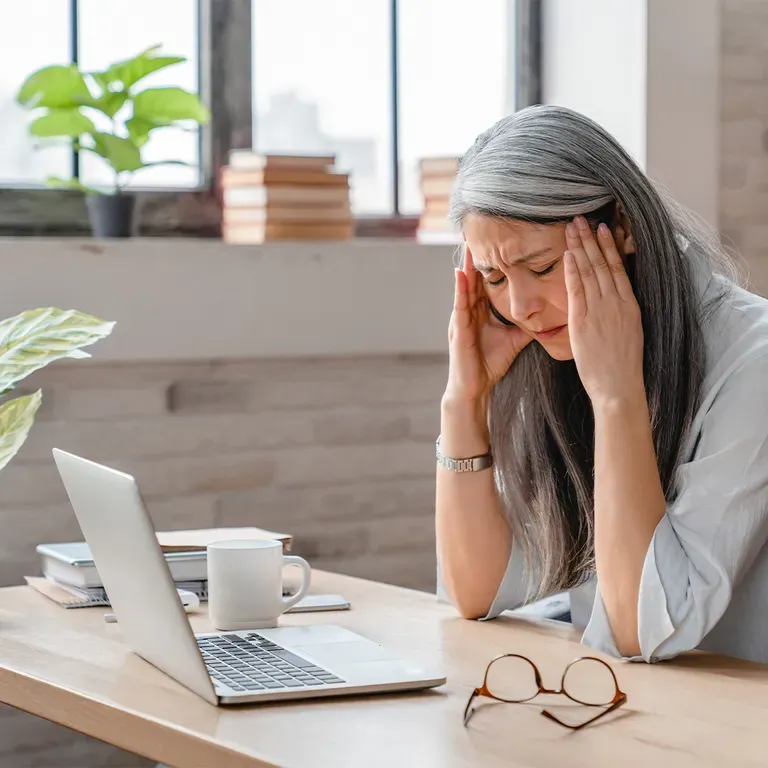 Woman sitting at desk holding head in pain.